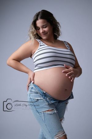 Pregnant woman in crop top and jeans cradling her baby bump during a maternity photo session. Newborn Photographer in Towne Lake