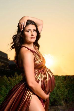 Pregnant woman in golden dress holding baby bump at sunset. Maternity Photographer in Cypress TX | Luxury Baby Photography