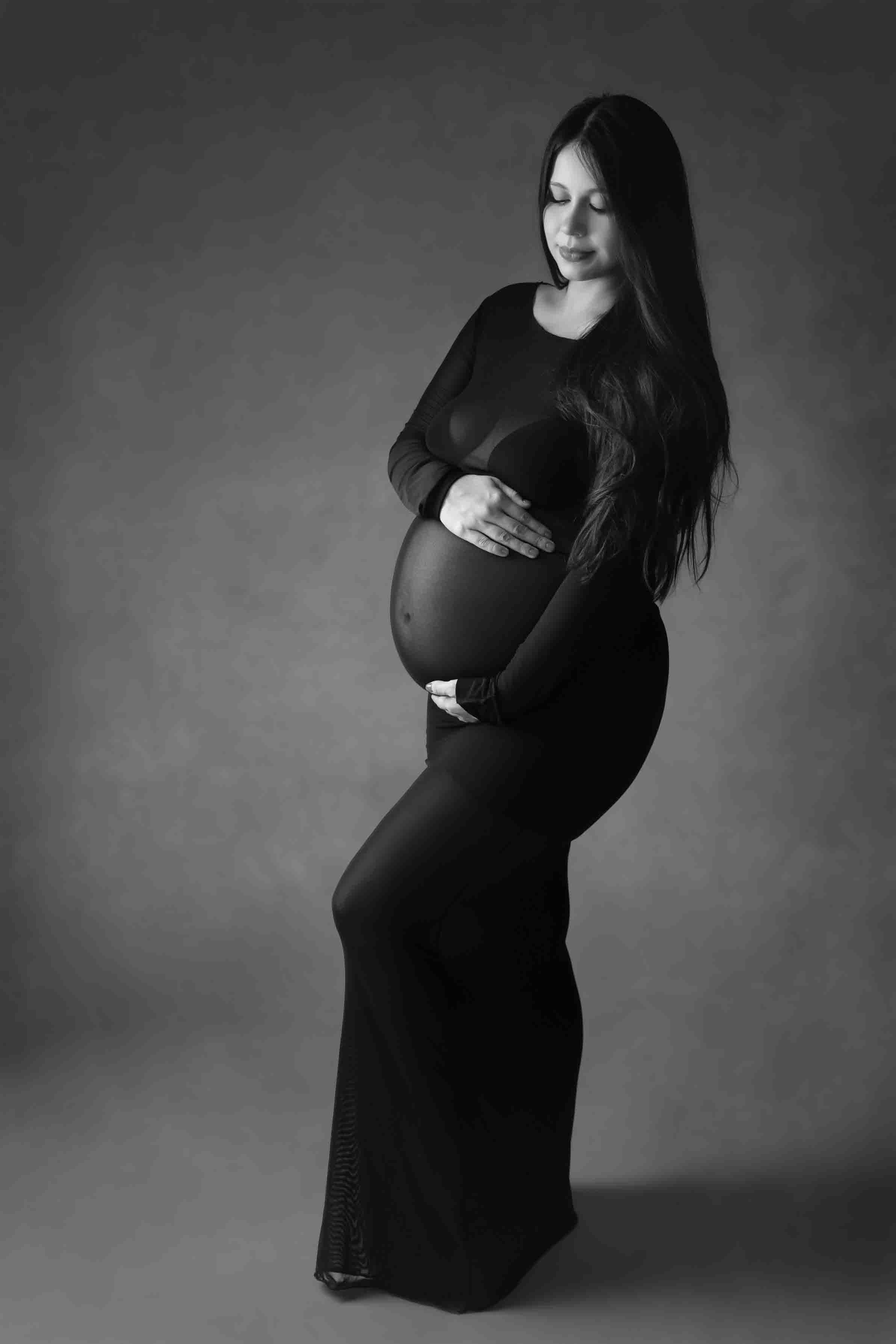 Black and white maternity of a pregnant  in a black dress cradling her babybump in a studio setting. fine art maternity photographer Cypress