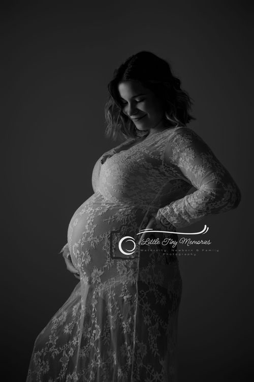 Black and white maternity photo of a smiling pregnant woman in lace gown cradling her baby bump.  Cypress TX Maternity Photographer
