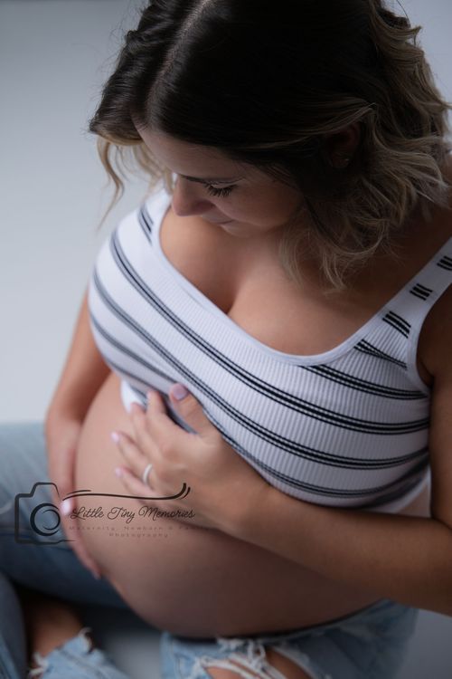 Pregnant woman in striped top cradling baby bump, looking down lovingly during maternity photo session. studio maternity photoshoot cypress