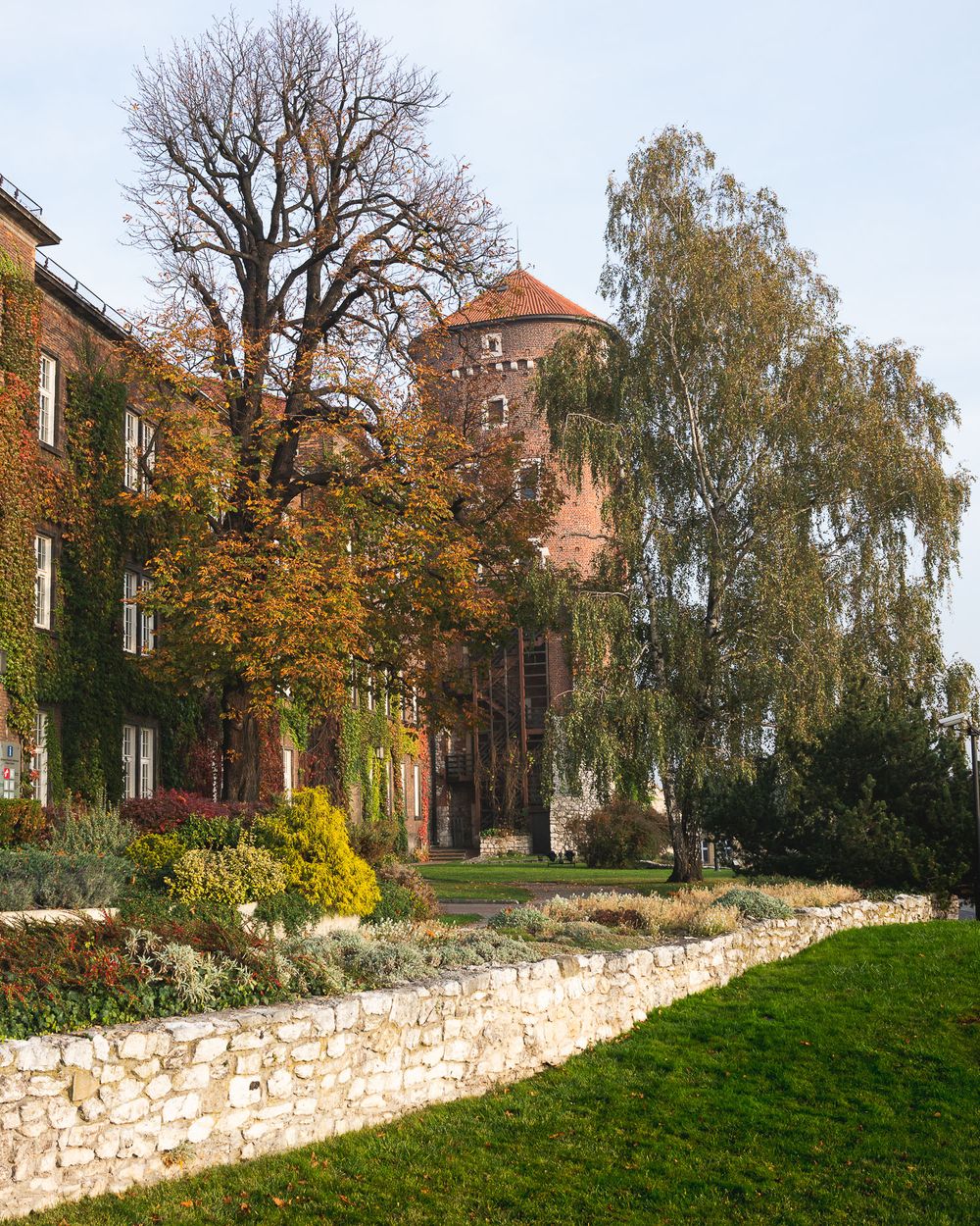 Historic brick building with autumn trees and stone wall on landscaped grounds.