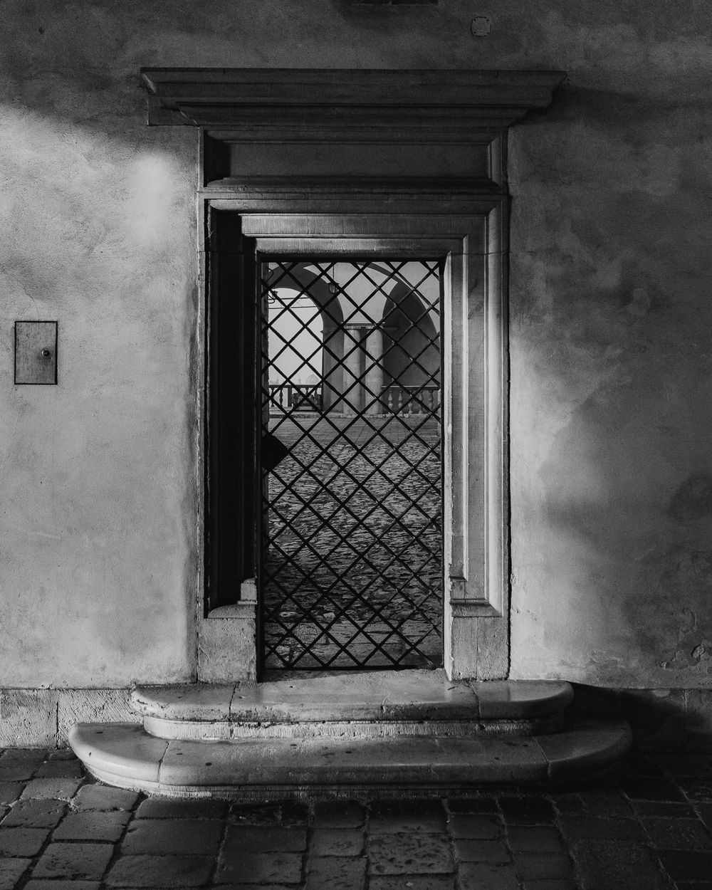 Black and white architectural detail showing a series of gothic windows with diamond lattice patterns in a stone wall.