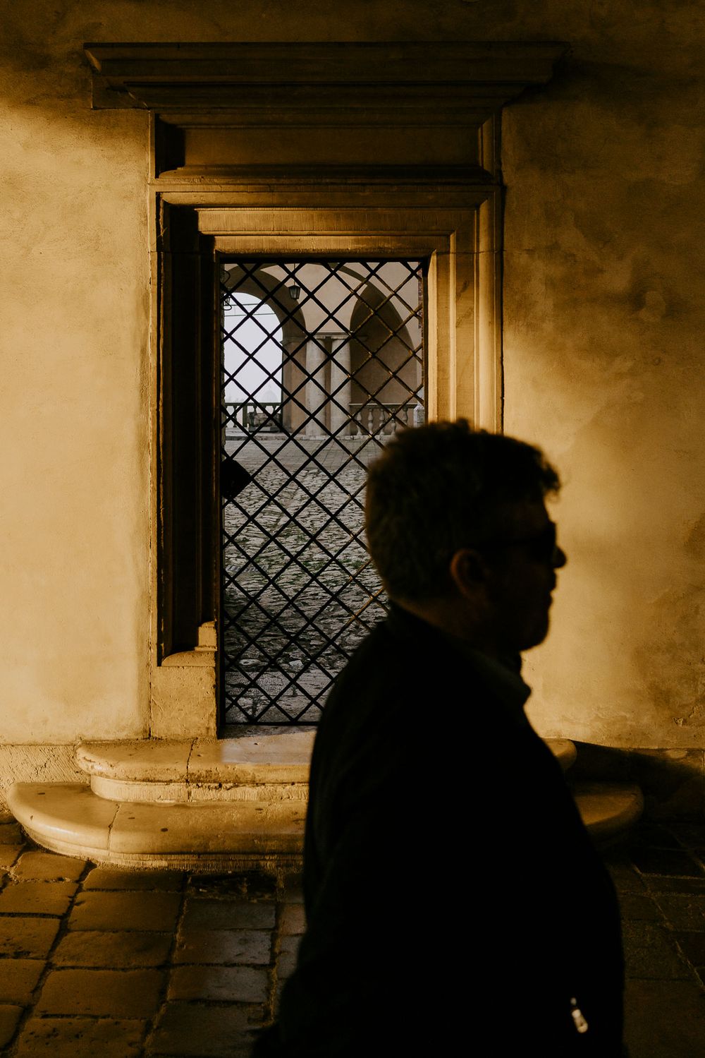 Silhouette against grated window in atmospheric stone hallway.