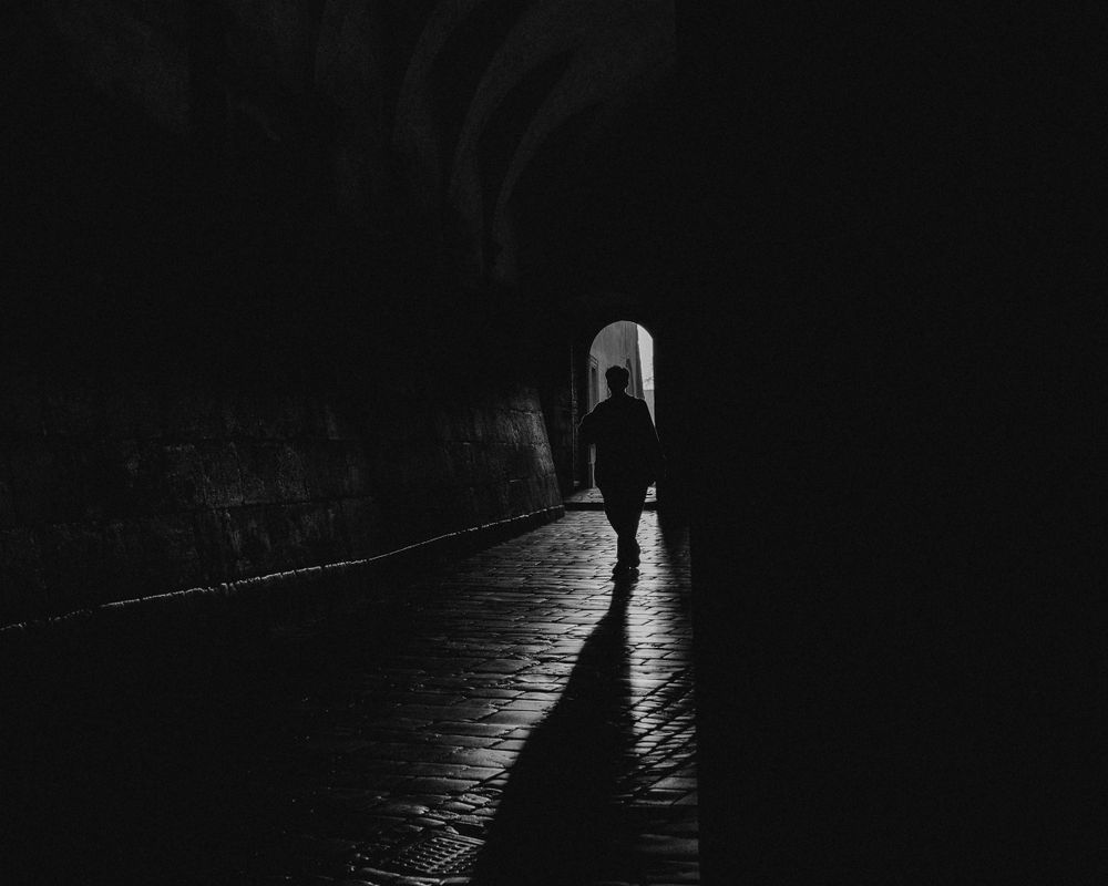 Silhouetted figure walking through dark tunnel towards distant light.