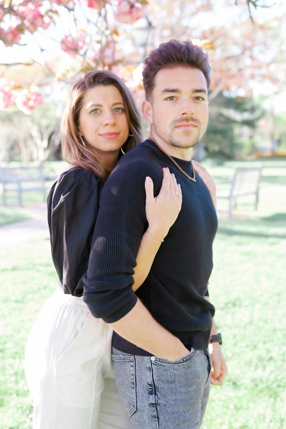 Couple in matching black outfits embraces on grassy hill during autumn photo session.