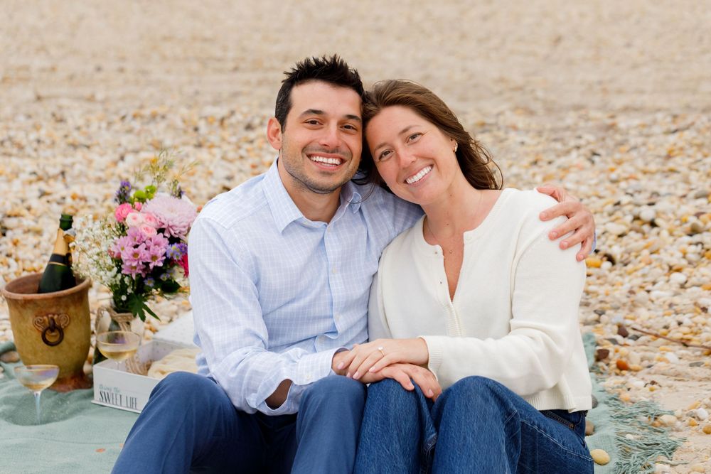A couple enjoying a romantic beach picnic with flowers and champagne.
