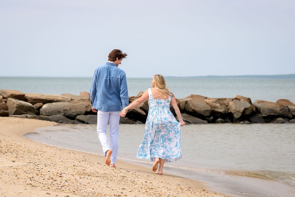 A couple walking hand in hand along a rocky beach shoreline.