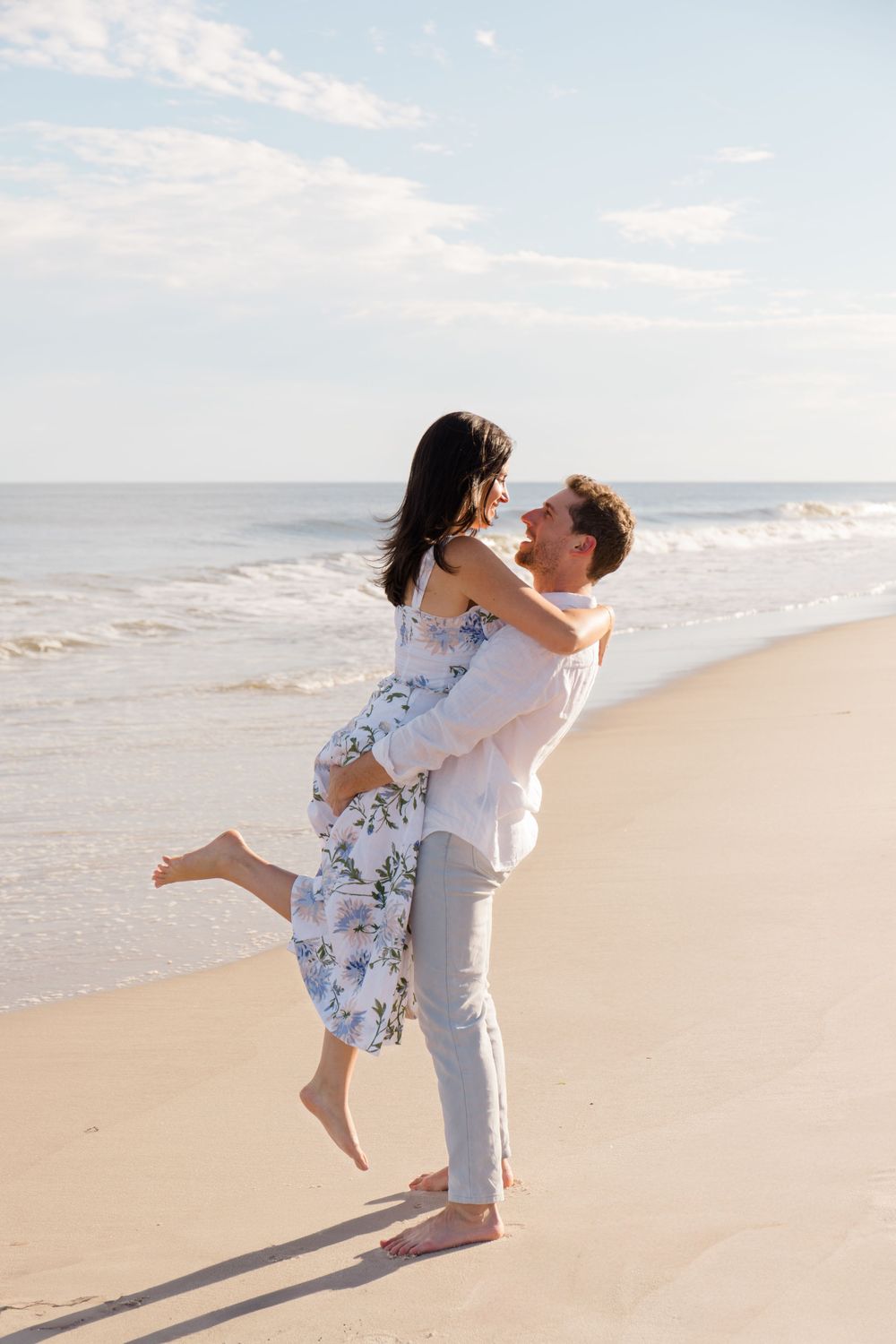 Playful couple embraces and spins on an empty beach during golden hour.