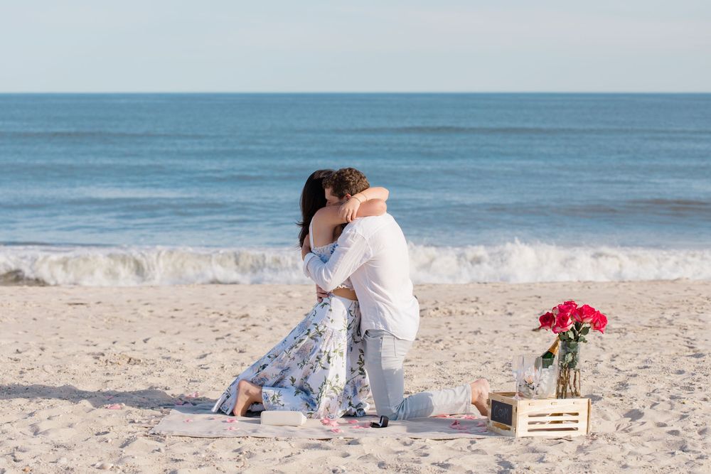 A beach proposal scene with wooden crates and red flowers on the sand.