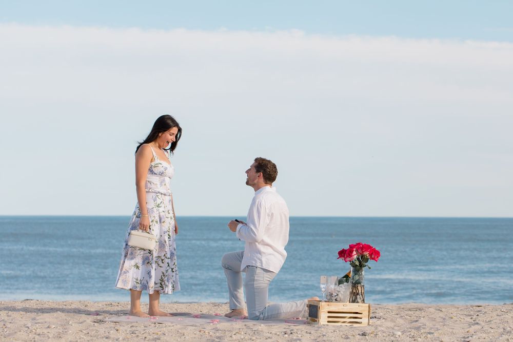 A beachside proposal moment with decorative wooden crates and red roses.