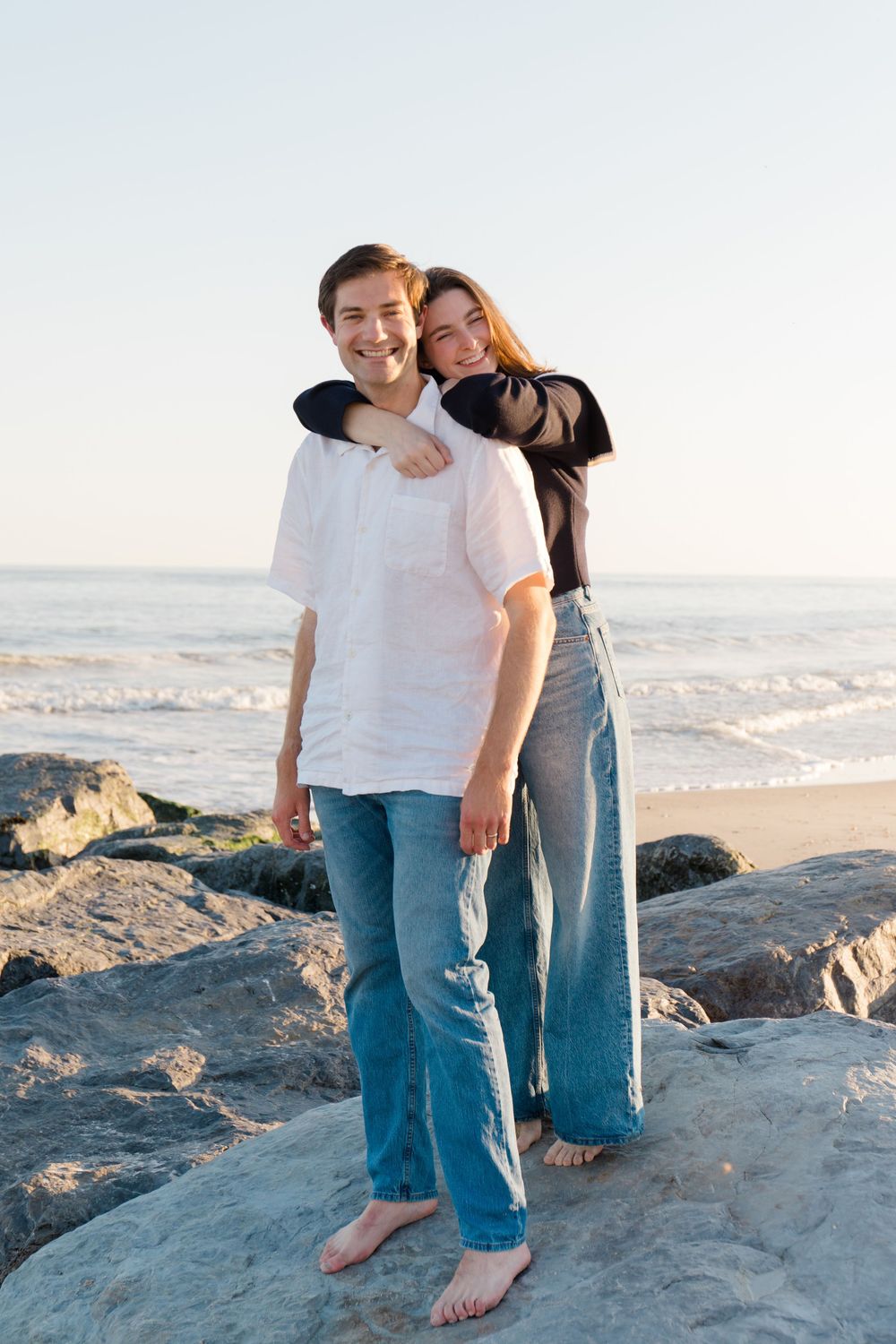 Couple sharing a romantic moment together on rocky beach during sunset.