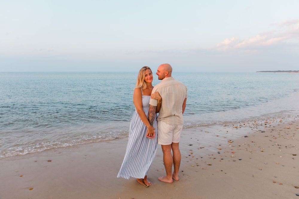 Couple in white and blue outfits sharing intimate moment on beach.