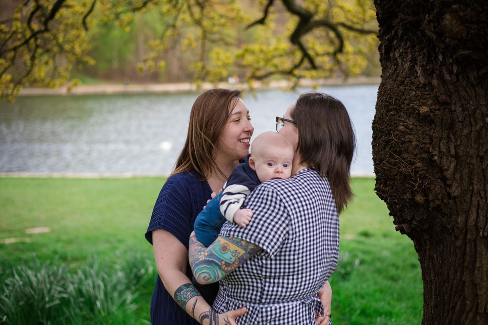 Three people share a joyful moment together under a tree by a lake.