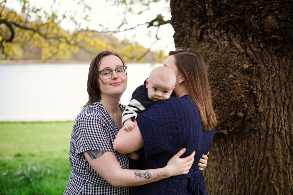 Family of three embraces by a tree with a lake in the background.