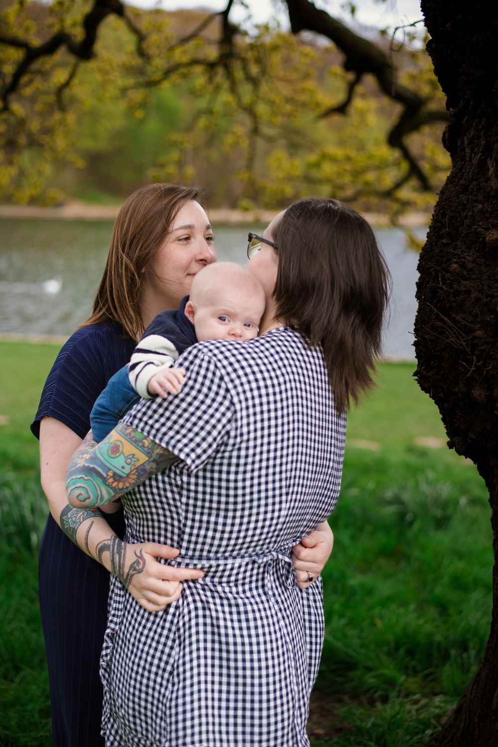 Two adults share intimate moment with baby between them near water.