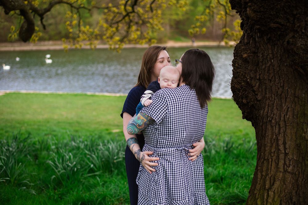 Couple shares tender moment with infant by lakeside under autumn tree.