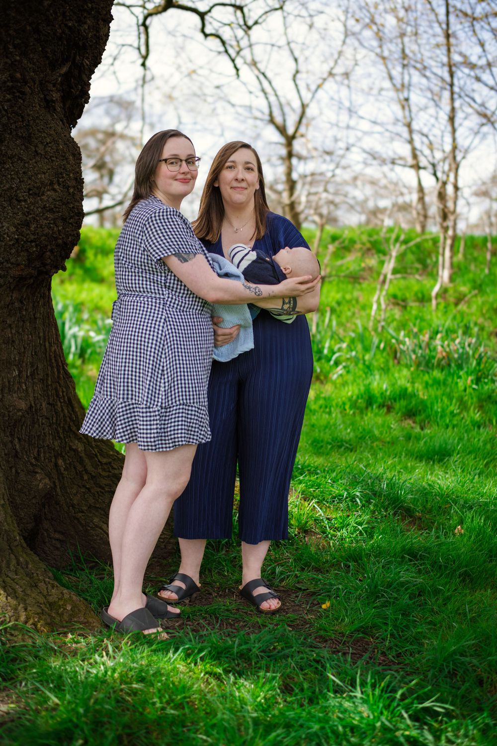 A couple in matching navy and gingham dresses stand together by a tree in a spring garden.