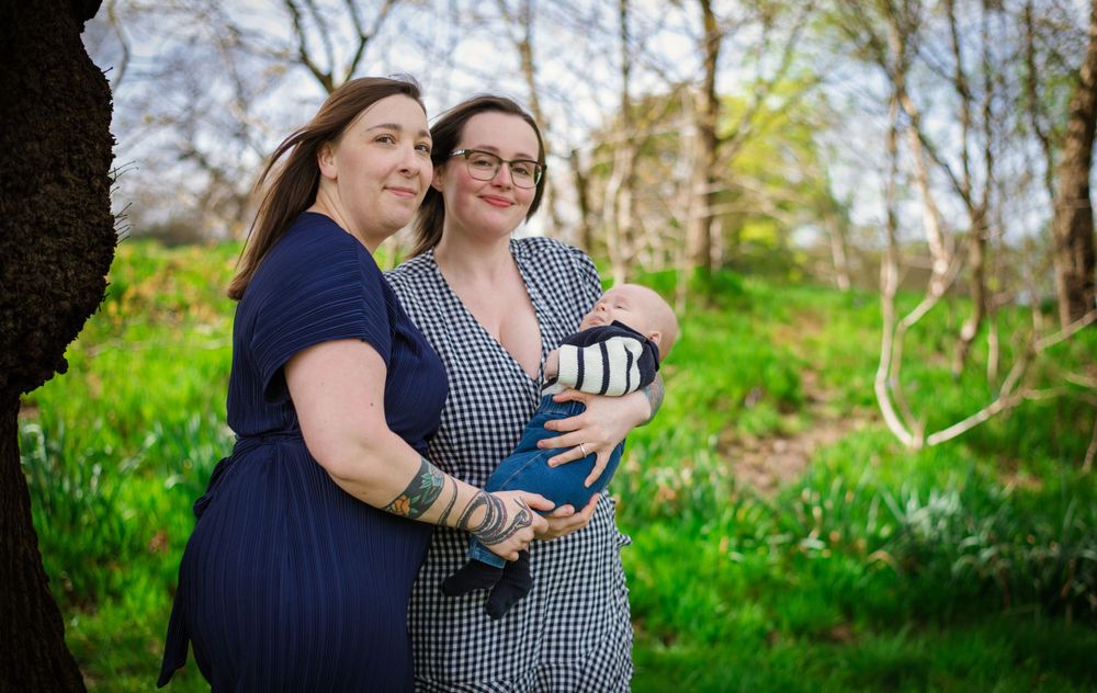 Two adults stand together holding a baby against a scenic spring background.