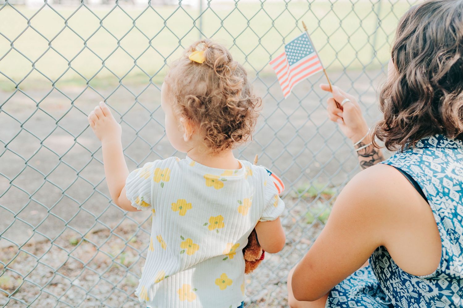 Child and adult wave small American flags through chain link fence.