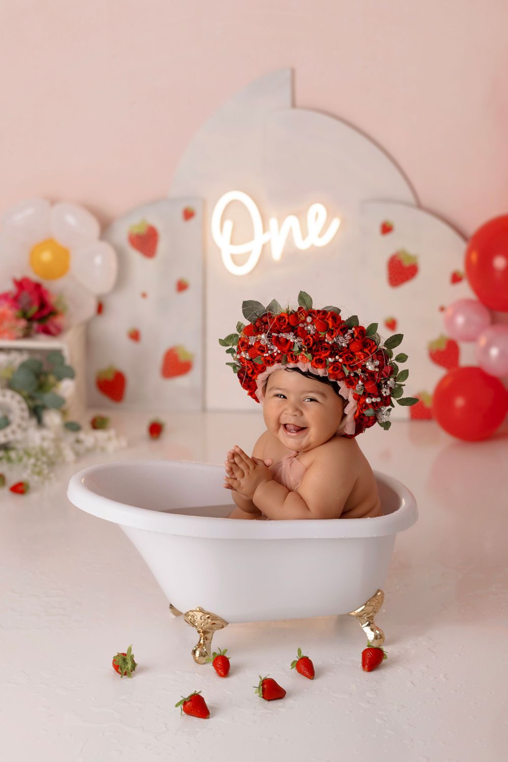 Festive bath photoshoot with strawberry crown and white clawfoot tub surrounded by red balloons.