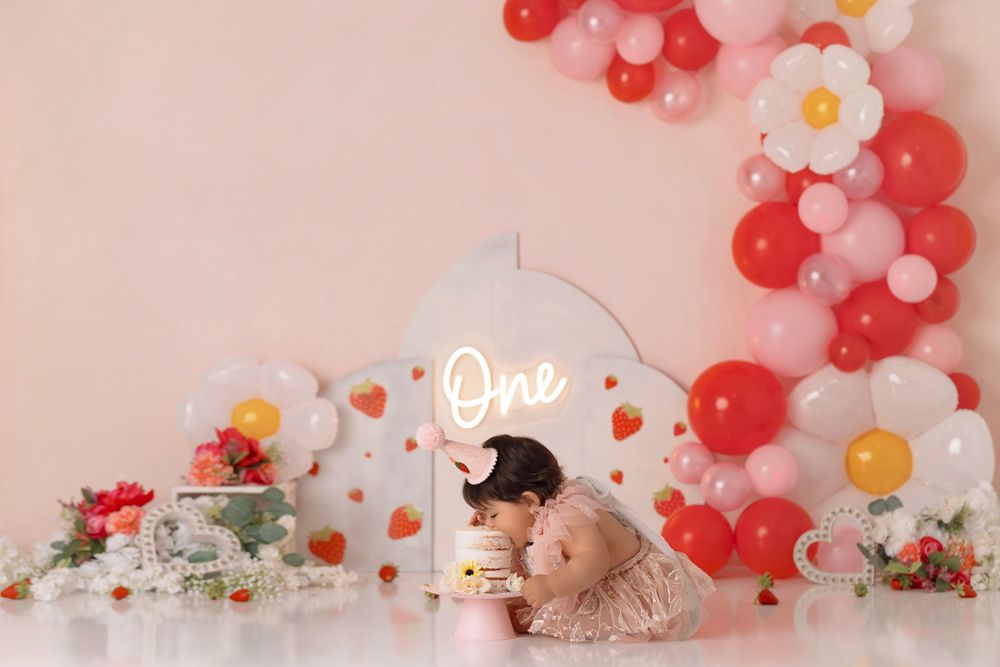 Sweet first birthday setup with neon sign, romantic balloon arch, and floral accents in shades of pink and red.