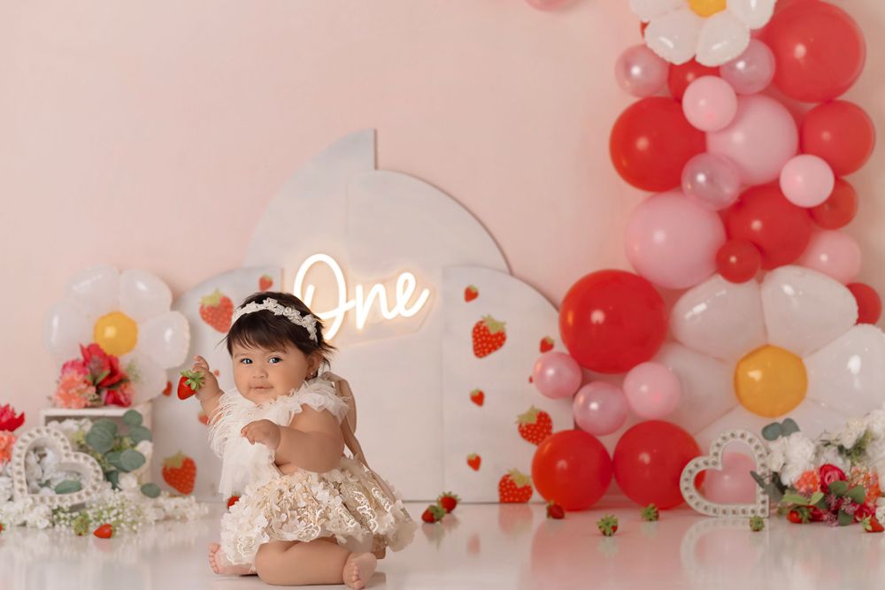 Birthday photoshoot with cream dress and balloon arch featuring red and pink balloons.