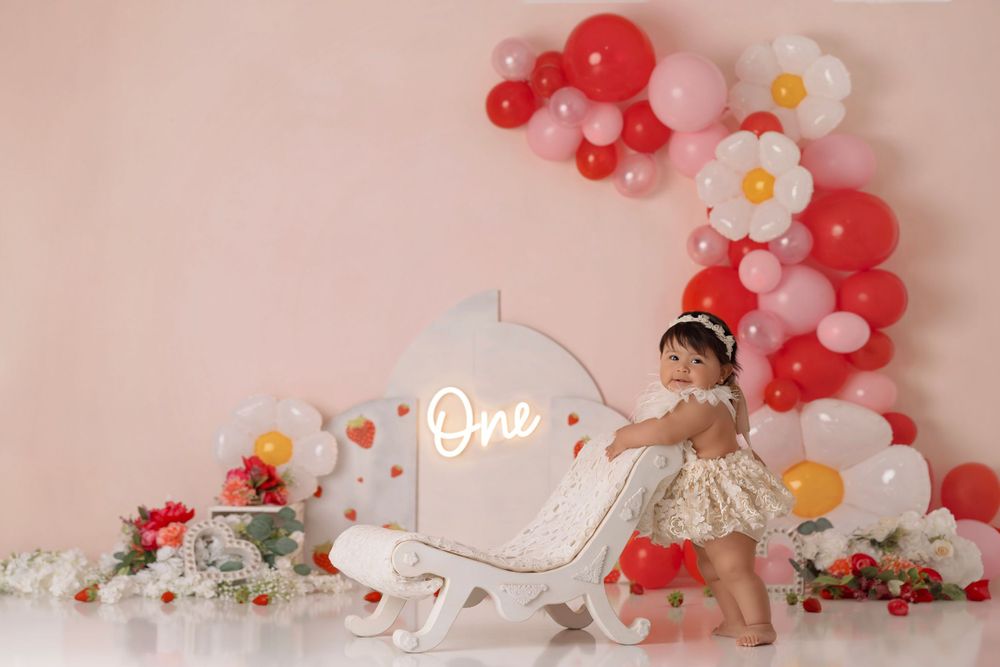 Birthday photoshoot with illuminated 'One' sign and red balloon arch decoration.
