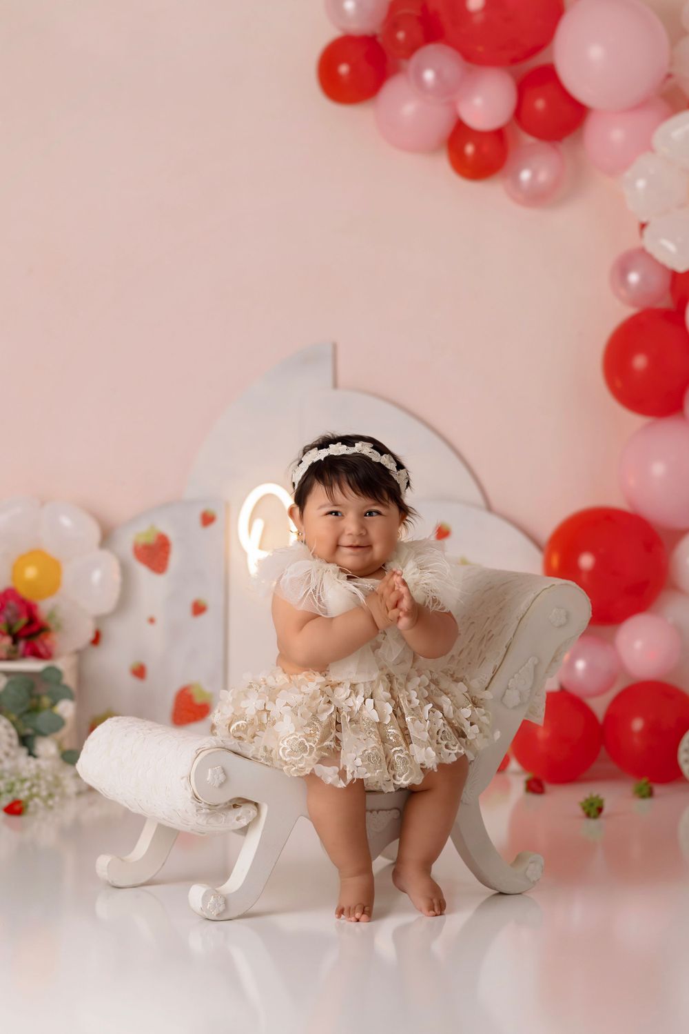 Elegant first birthday portrait with lace dress on white vintage chair.