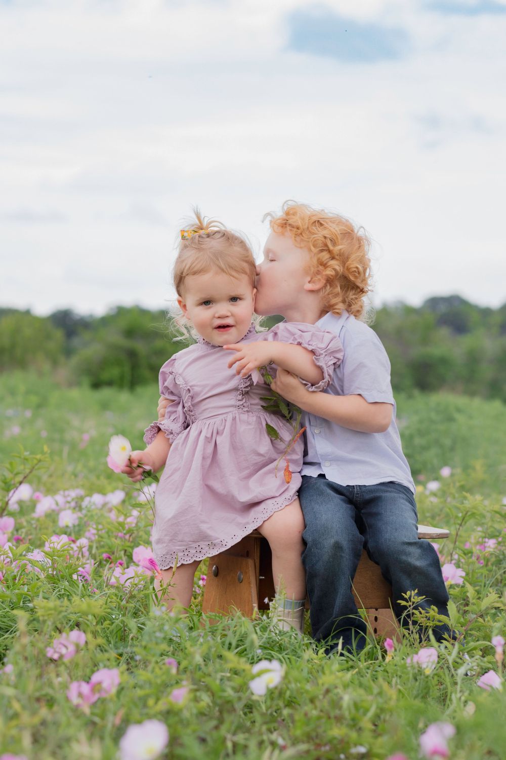 Two young children sit together on a wooden box in a wildflower meadow on a bright summer day. wildflower mini session