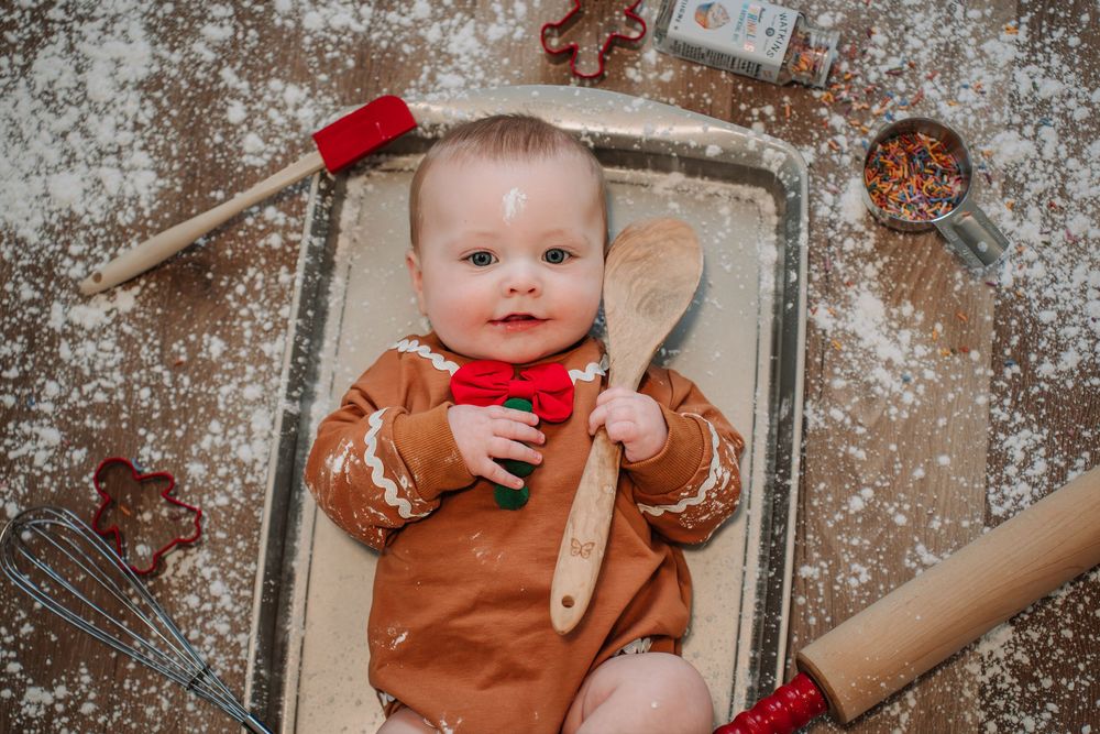 A child in a brown outfit plays with cookie dough and baking supplies on a flour-dusted surface.