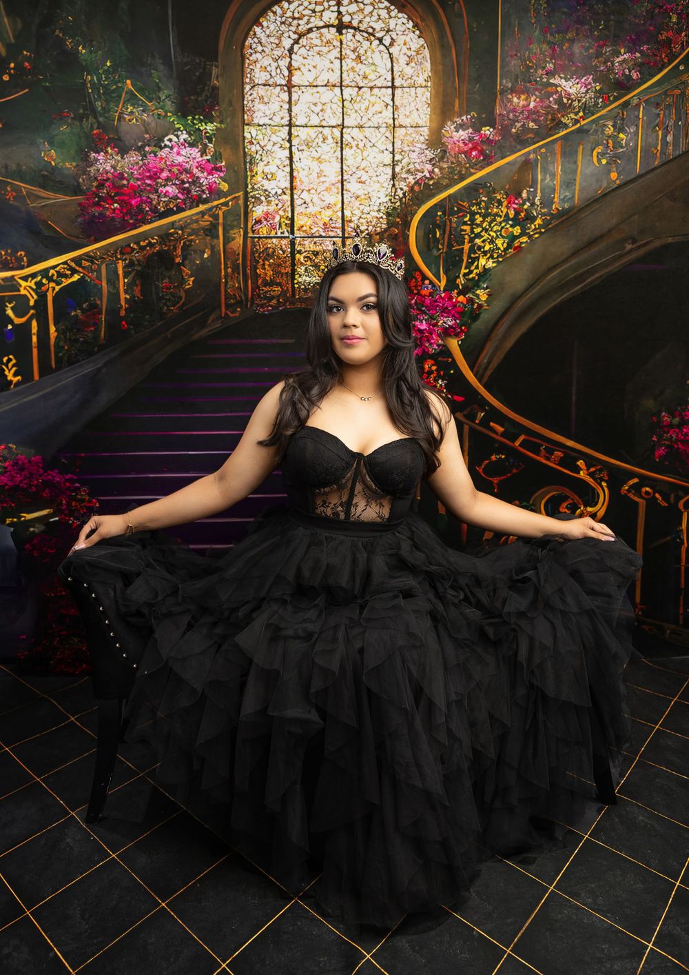 Elegant portrait in black ballgown on grand staircase with floral decorations.