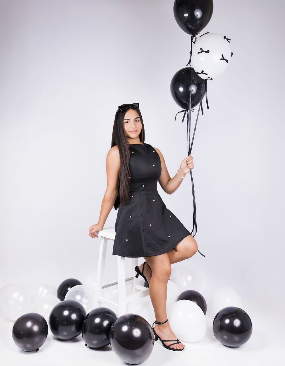 A model in a black dress poses with black balloons against a white backdrop for a stylish photoshoot.