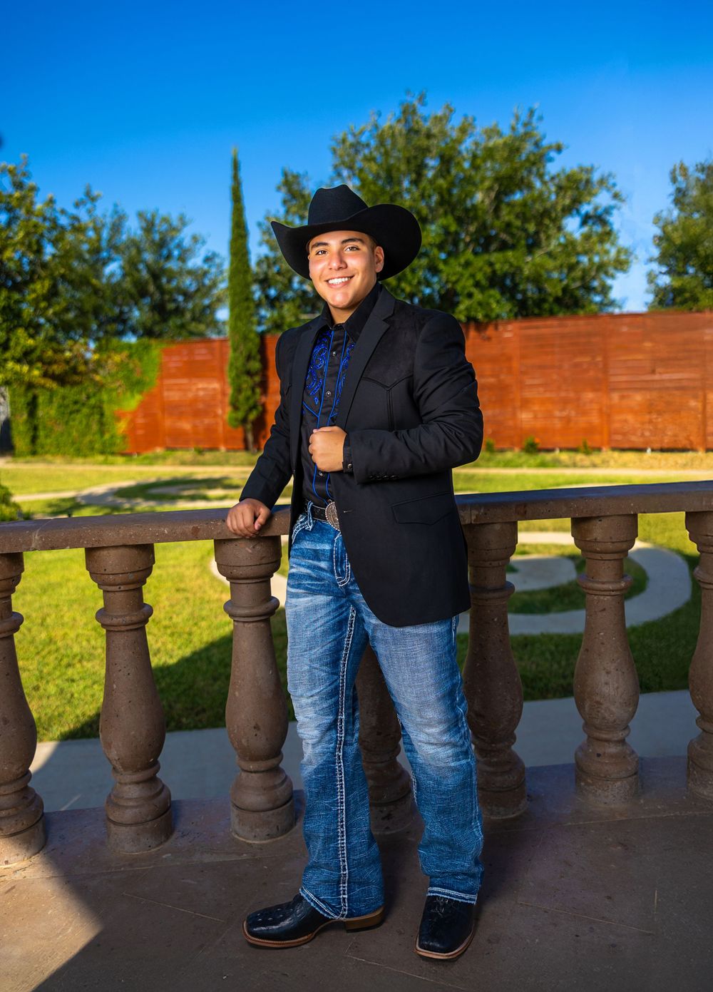 Person in blue jeans and black jacket standing by ornate stone balustrade at sunset against blue sky.