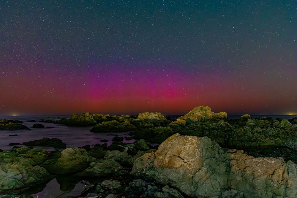 Aurora borealis illuminates rocky coastline with vibrant pink and purple hues against a starry night sky.