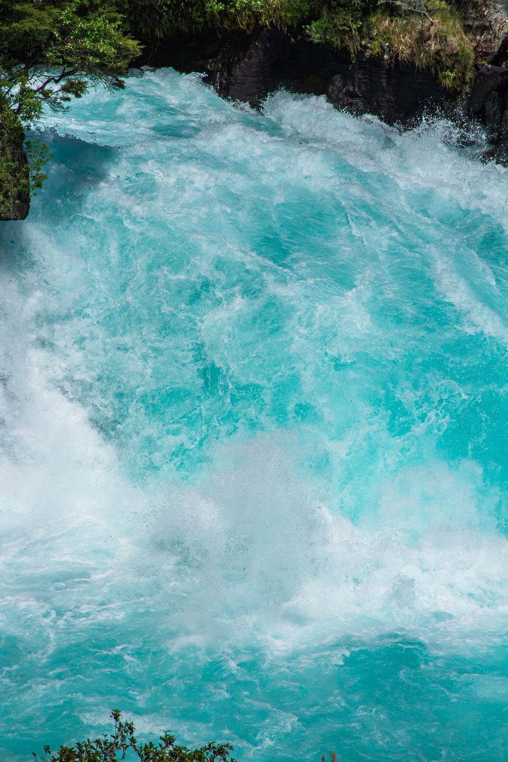 Turquoise glacial water churns and crashes through rapids creating dramatic white water patterns and foam.