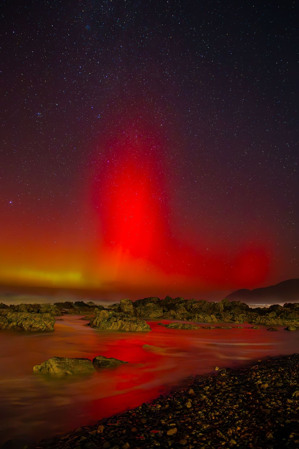 Red glowing volcanic activity illuminates a dark night sky over a rocky landscape in Hawaii.