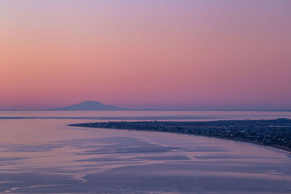 A serene coastal landscape at sunset with pink and purple hues reflecting off the calm ocean waters.