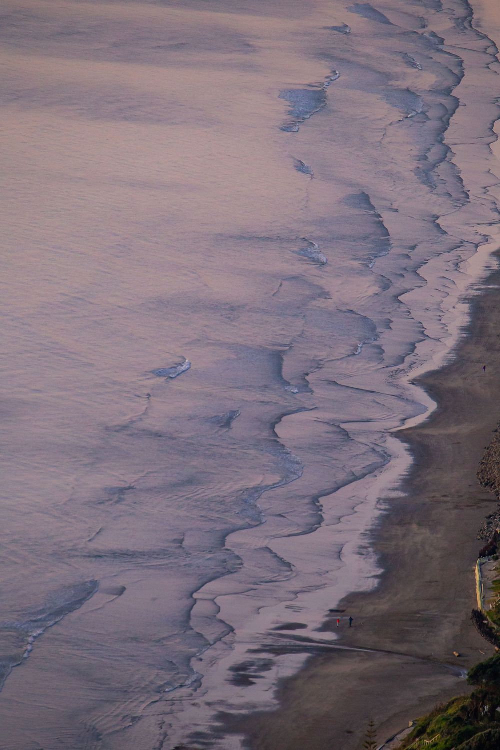 Aerial view of rippling ocean waves meeting the shoreline with dark sand beach stretching into the distance.