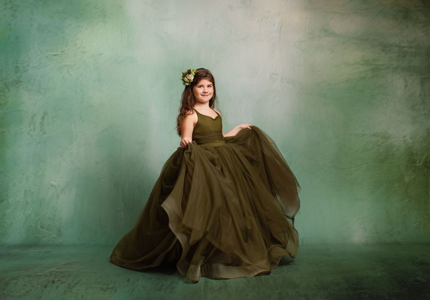 Ethereal portrait in flowing sage green ball gown against moody dark background.