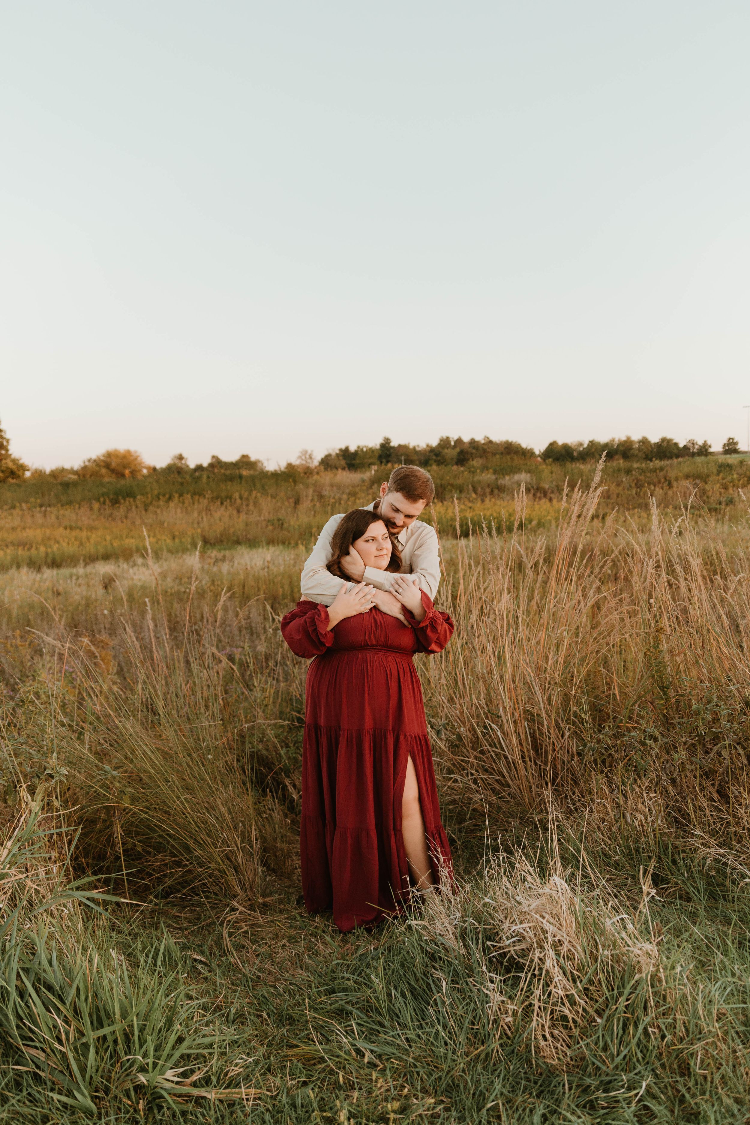 A romantic couple embraces in a golden field at sunset, with the woman wearing a flowing red dress.