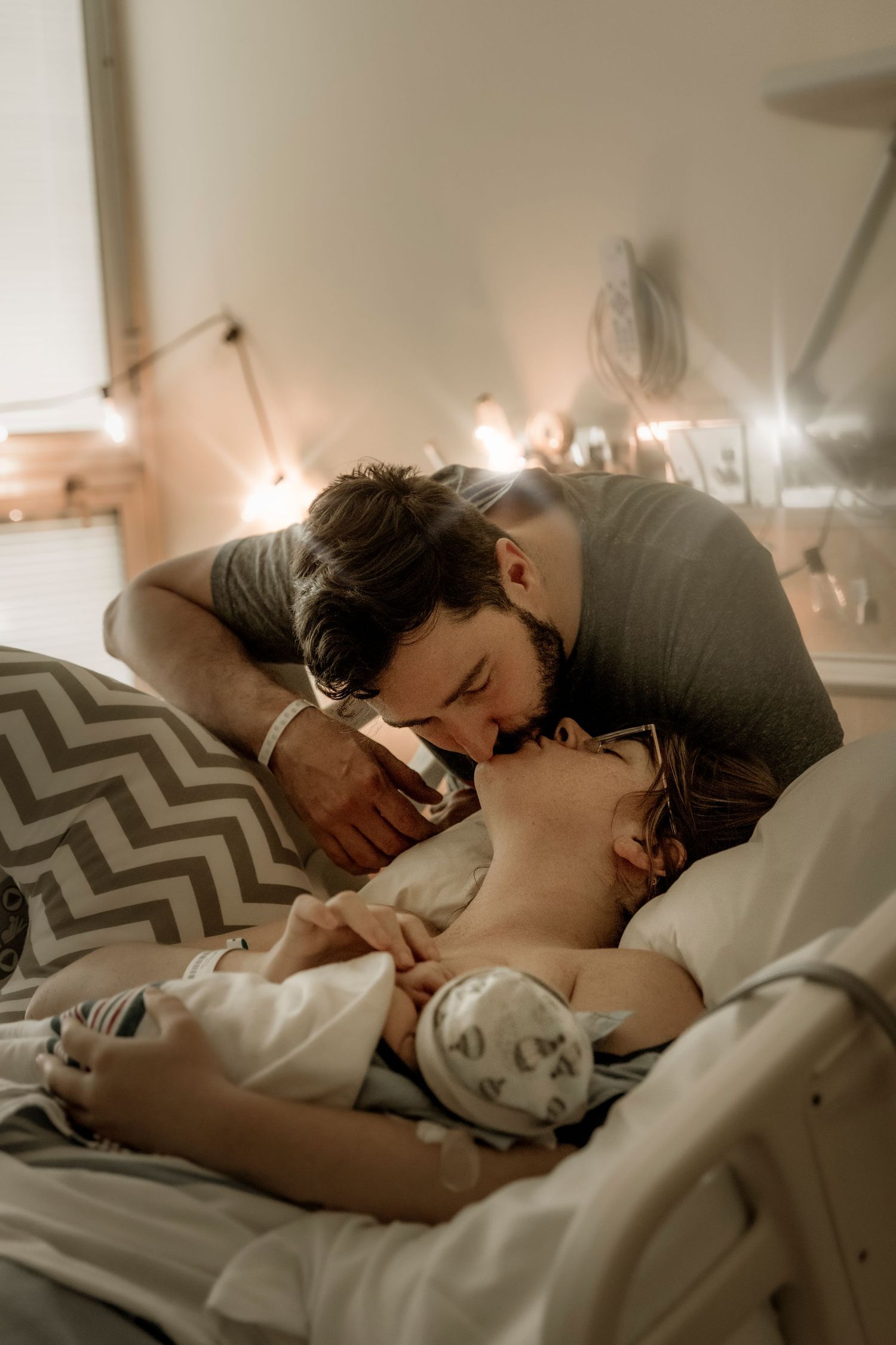 A romantic moment between a couple sharing an intimate embrace while lying on a bed with chevron pillows in soft lighting.