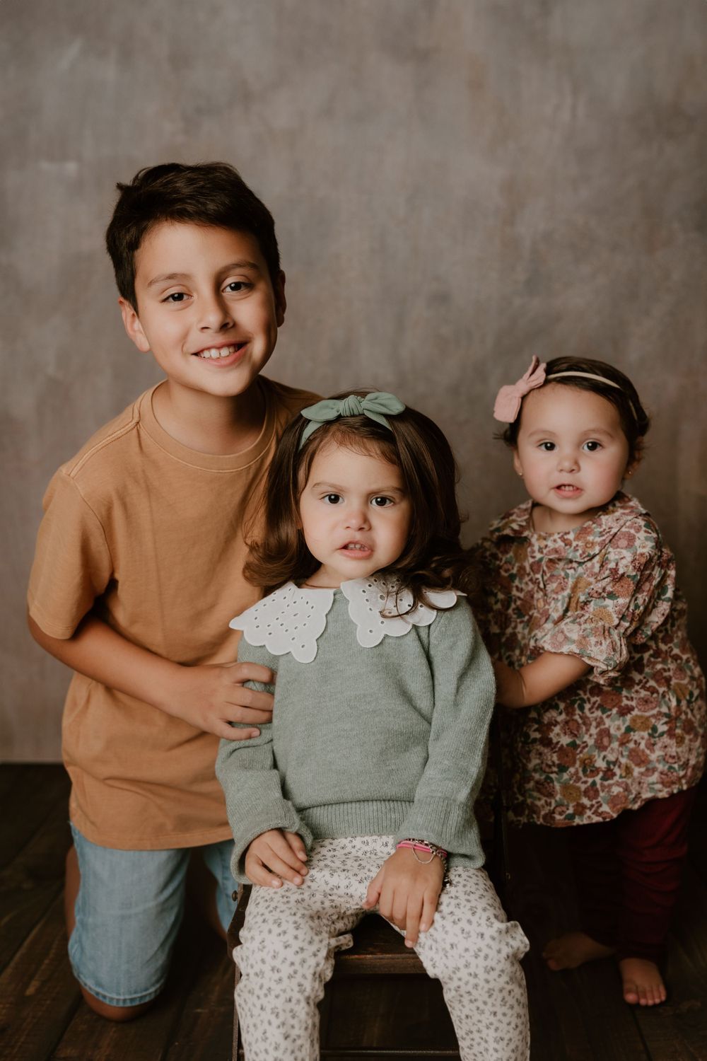 Studio portrait of three siblings in coordinating outfits against gray background.