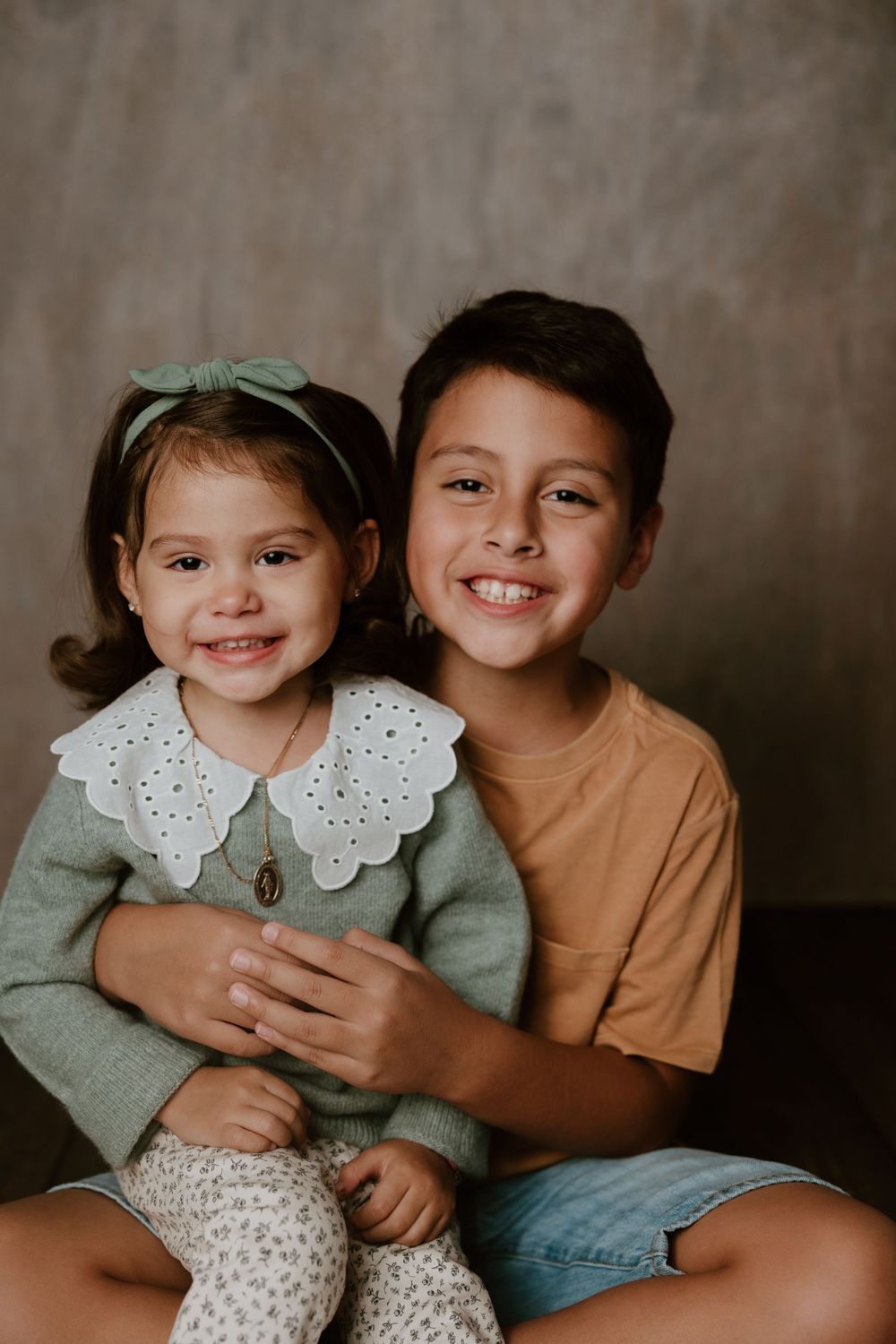 Studio portrait of siblings sitting together against gray background.