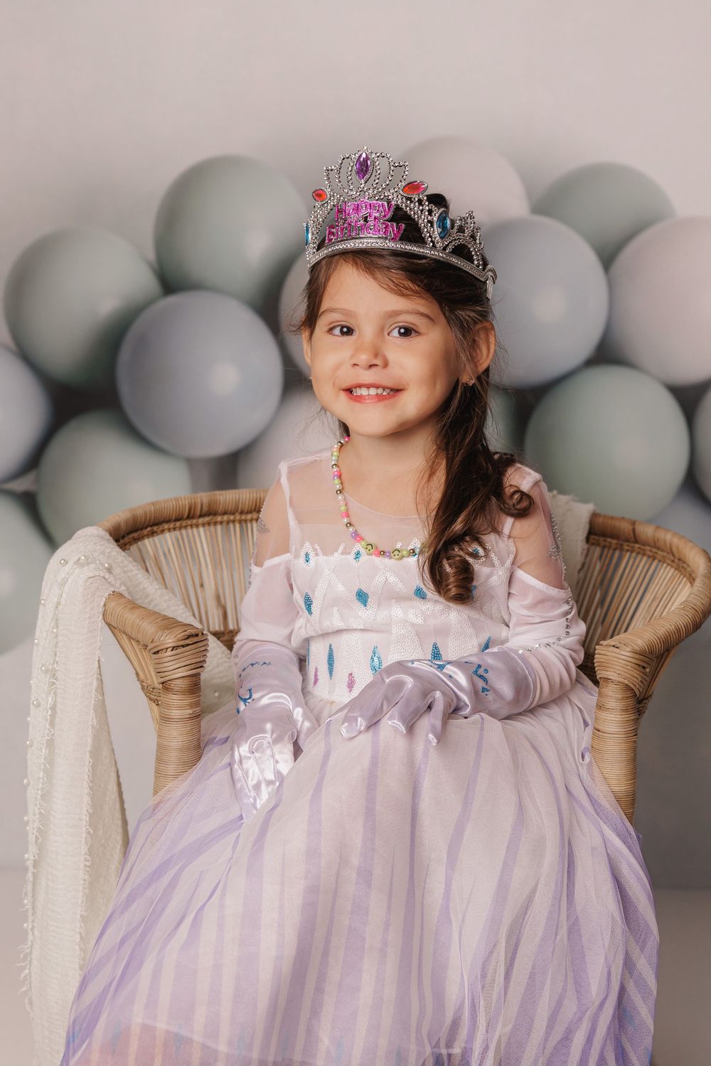 Princess themed portrait with silver balloons and a lavender tulle gown in a wicker chair.