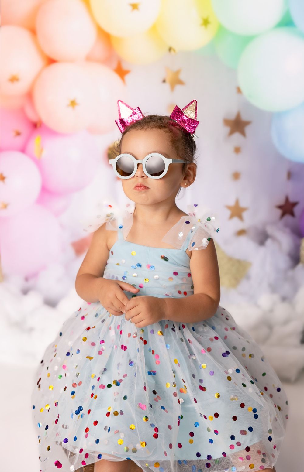Whimsical portrait with pastel balloon arch backdrop and sparkly dress.