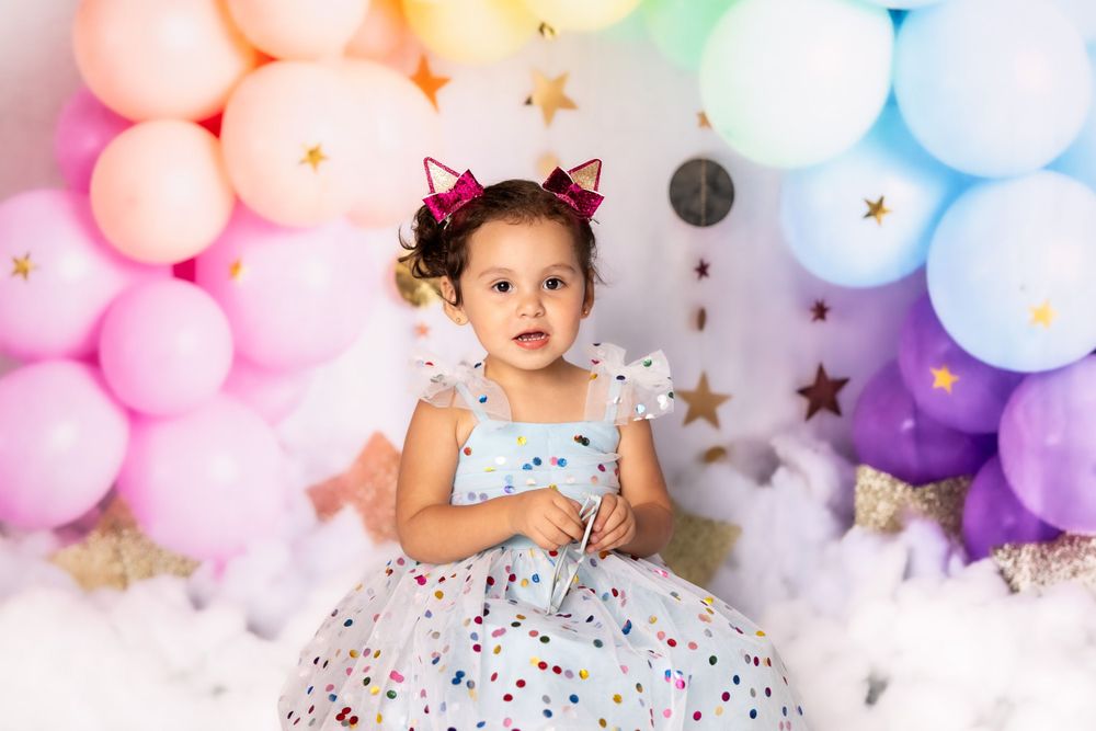 Festive portrait with rainbow balloon arch and confetti dress.