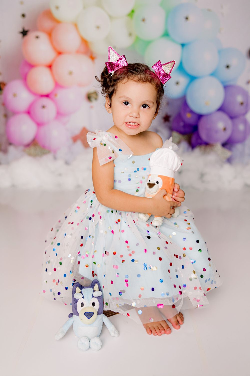 Festive portrait with pastel balloon arch backdrop featuring a dotted dress and pink hair bows.
