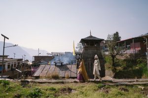 Hillside village scene with pagoda tower and mountains in background.