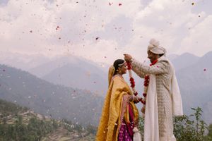 Traditional Indian wedding ceremony with flower petals falling against mountain landscape.